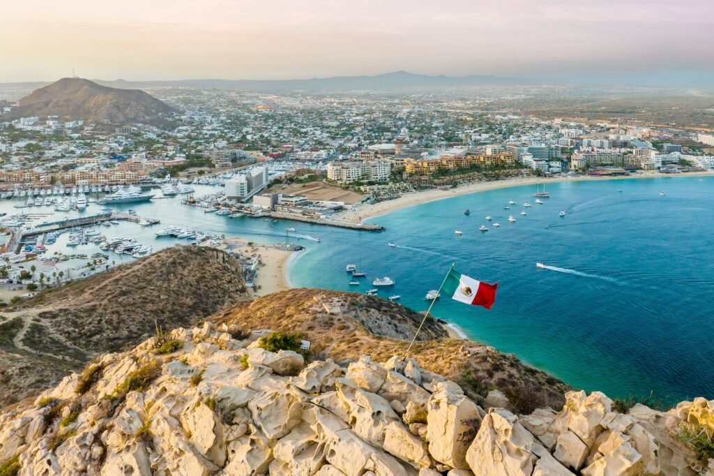 Vibrant flag waving in the foreground of a picturesque cityscape. Cabo San Lucas, Mexico.